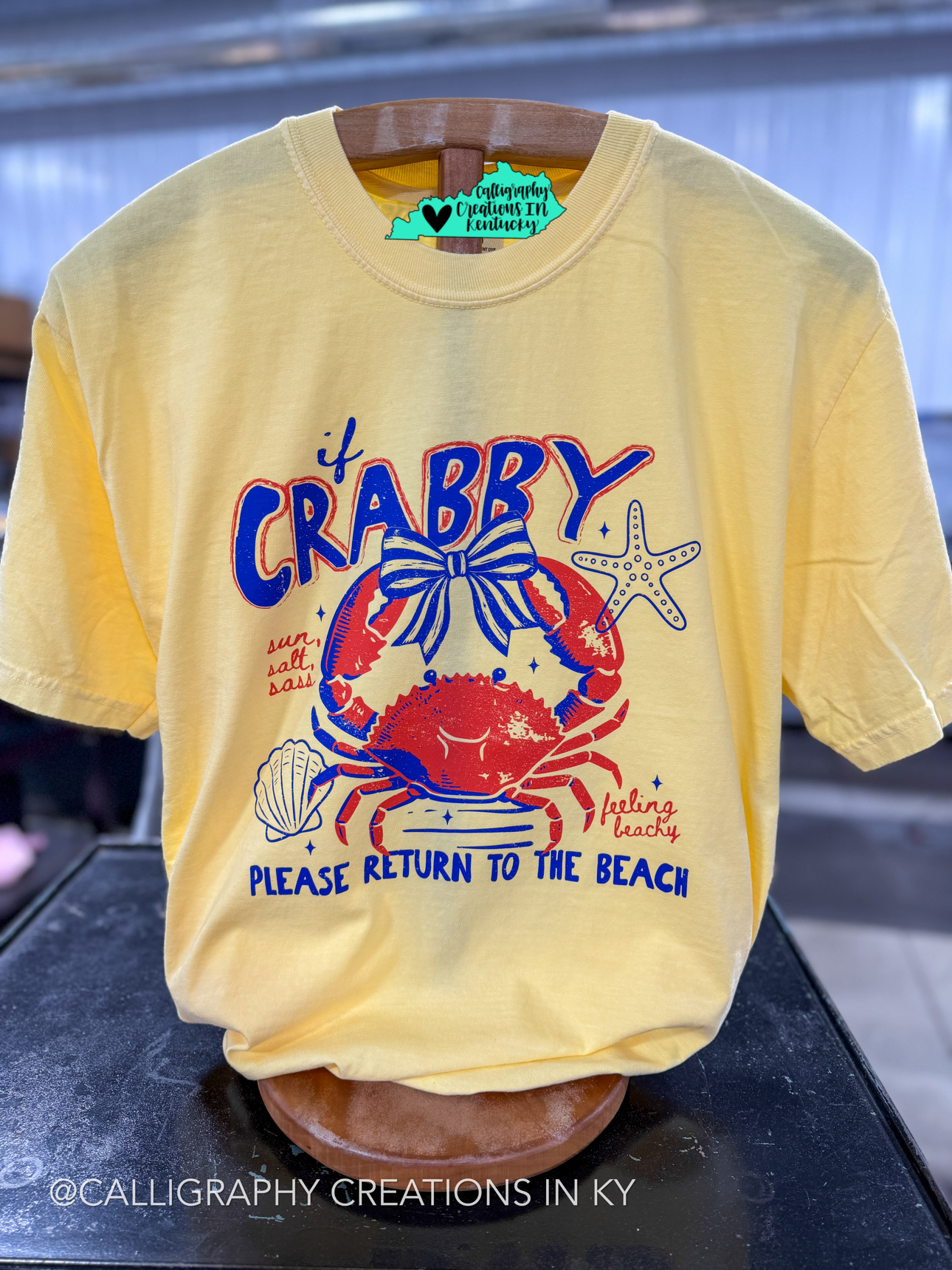 Yellow t-shirt with a red crab graphic and text on a black surface.