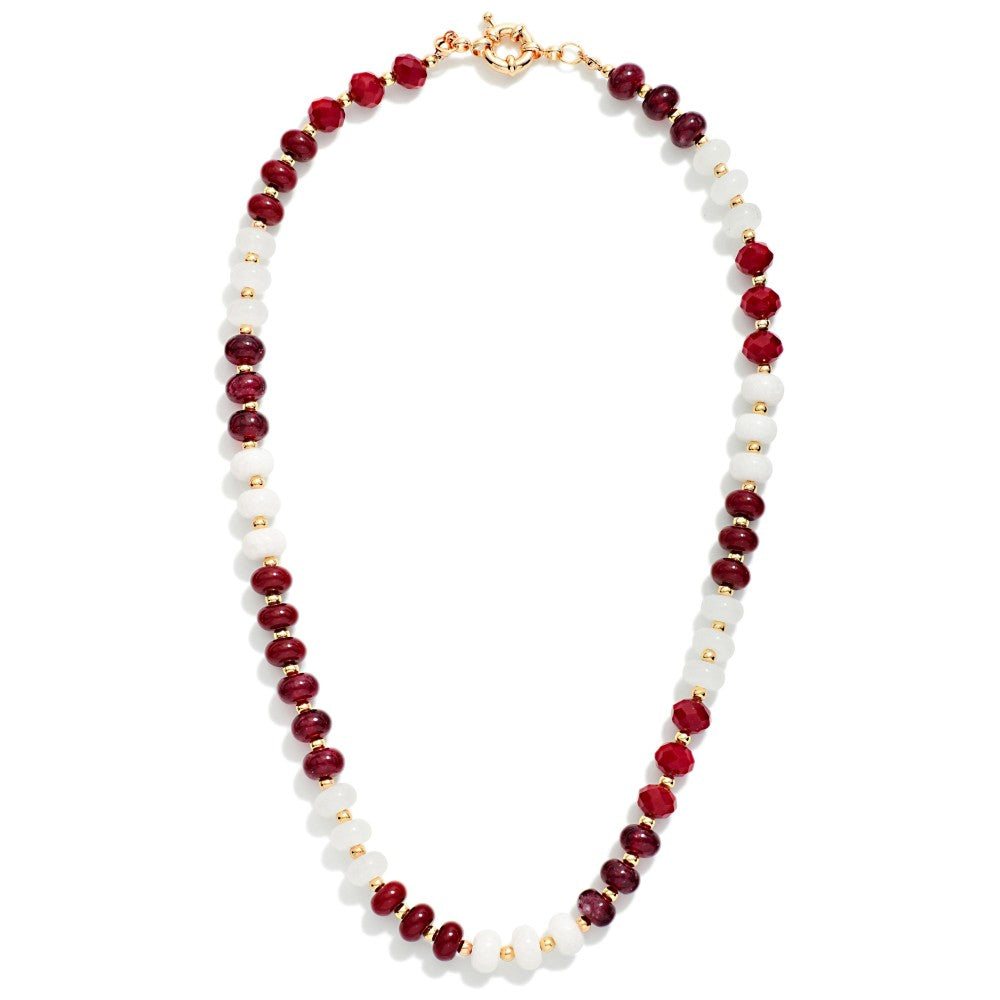 A beaded necklace featuring alternating deep red faceted beads and smooth white oval beads, separated by small gold spacer beads, with a gold clasp at the top, shown on a plain white background.