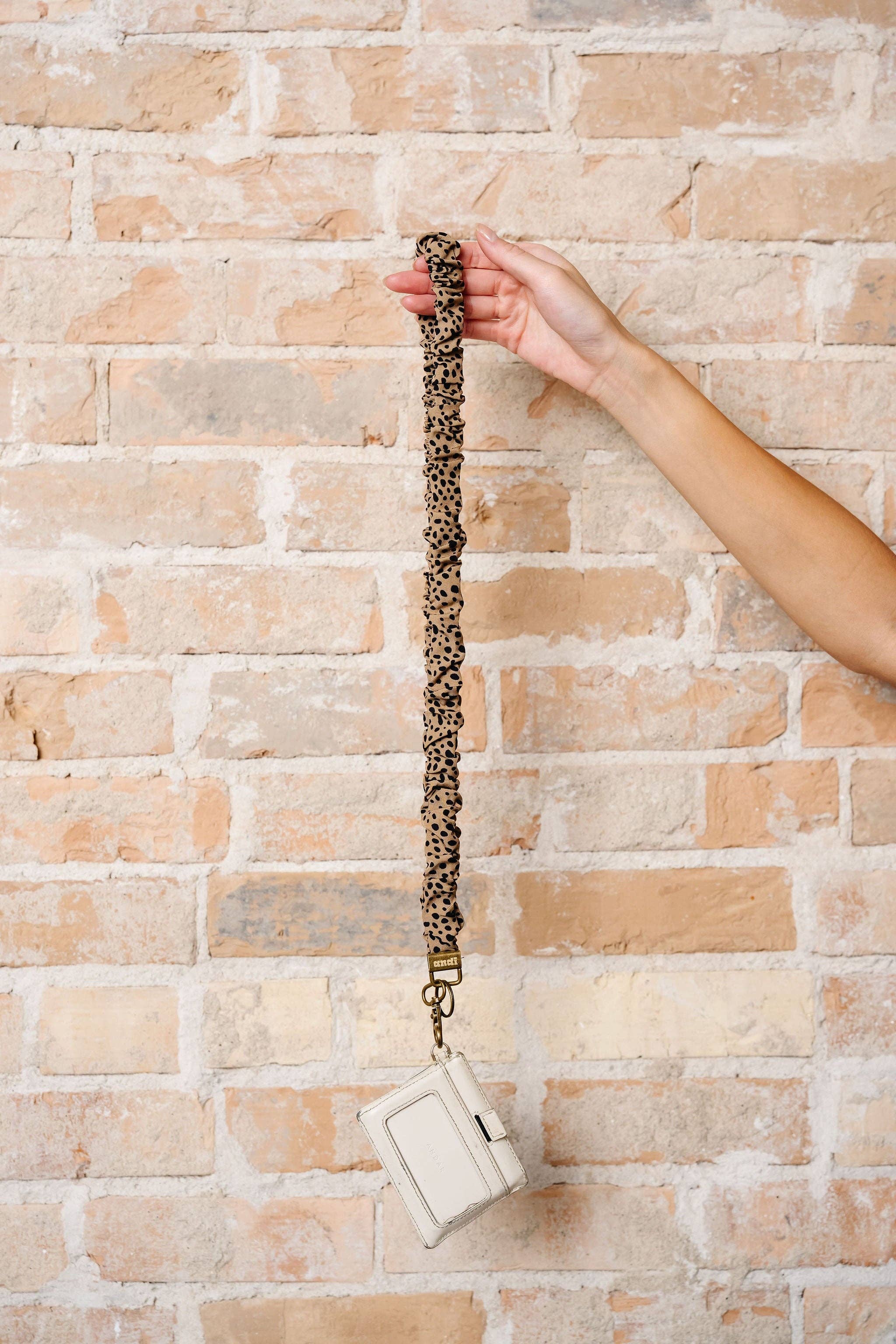 Brown lanyard with black spots with a white wallet attached against a brick background 