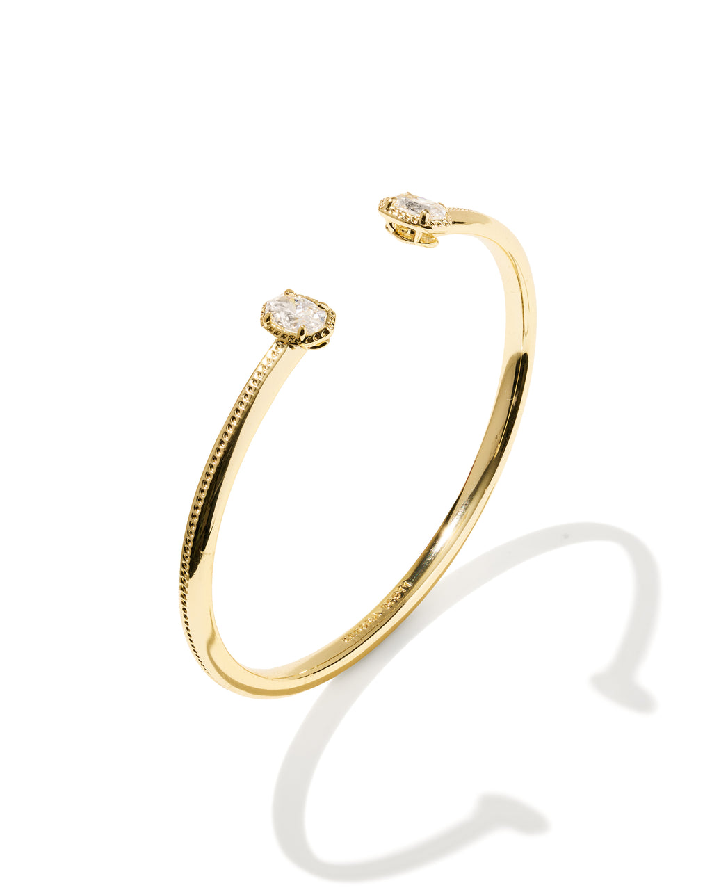 A gold open cuff bracelet with two small oval diamond settings, shown on a clean white background with a soft shadow.