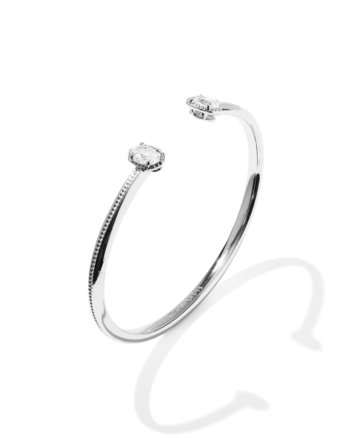 A silver-toned open cuff bracelet with two small round clear gemstones, photographed on a clean white background with a soft shadow.