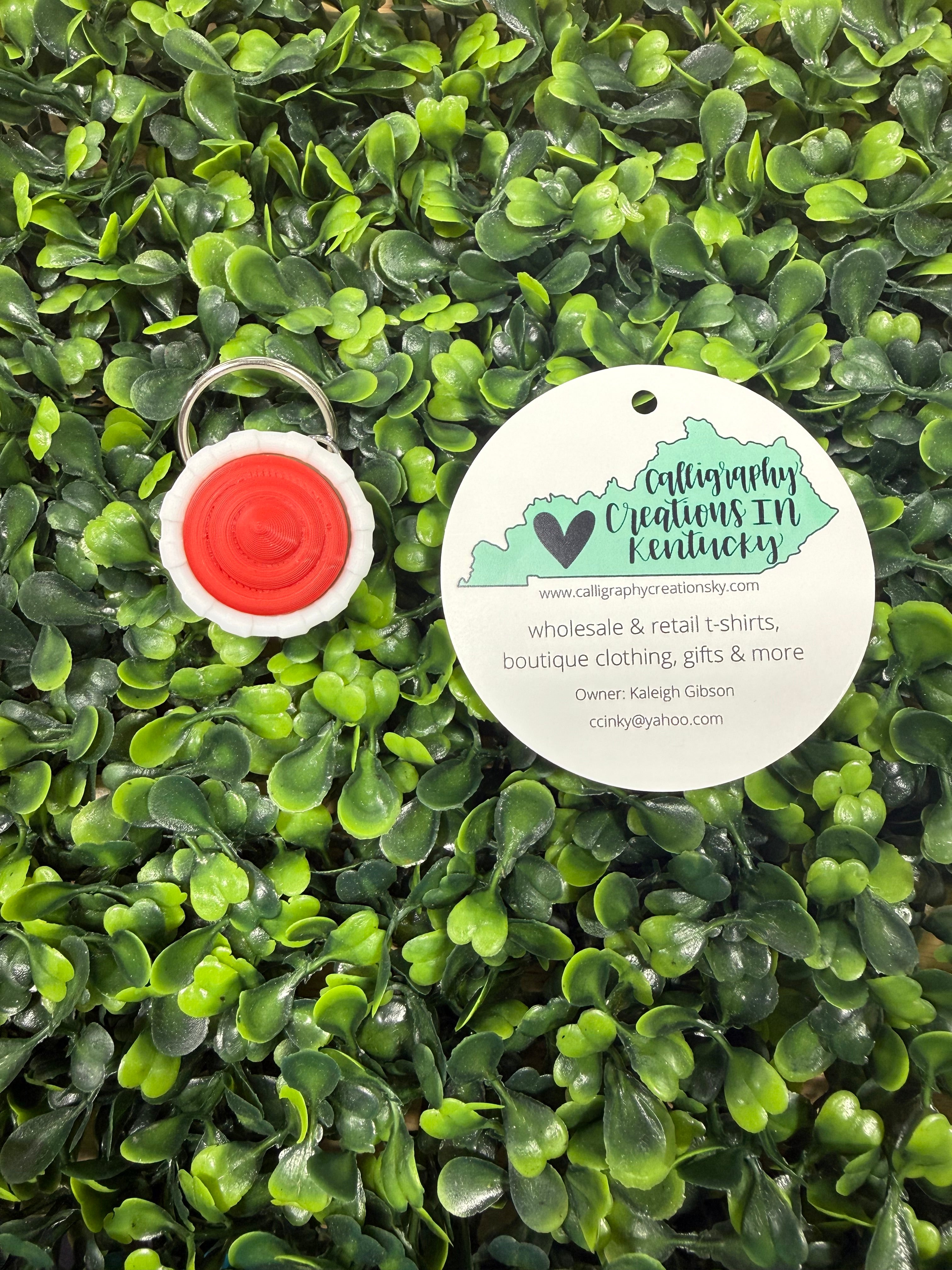Ketchup cup keychain on green artificial grass with a brand tag.