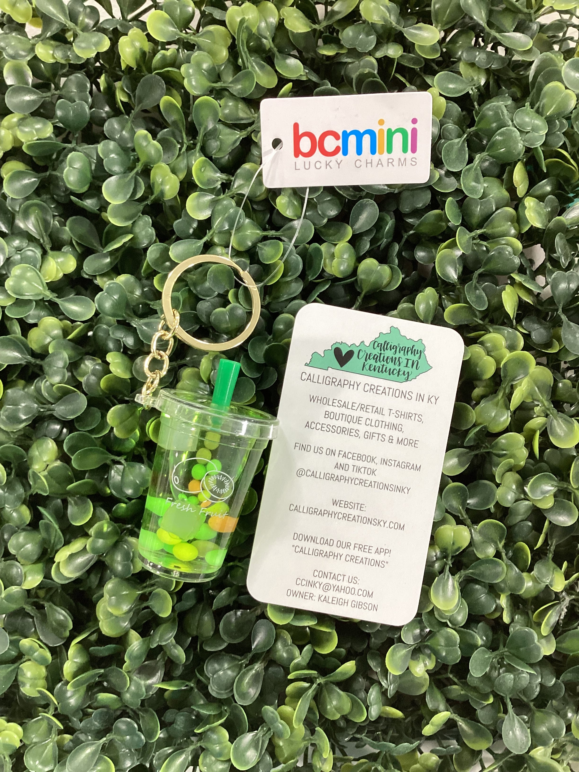Keychain with a small cup and green items on a green leafy background, featuring 'bcmini' branding.
