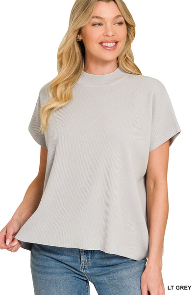Woman wearing a light gray short-sleeve top and blue jeans on a white background