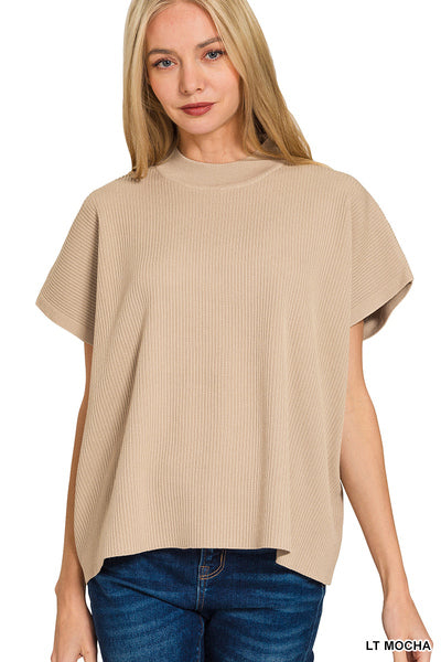 A woman wearing a light mocha beige short-sleeve ribbed knit top with blue jeans, shown against a plain white background.