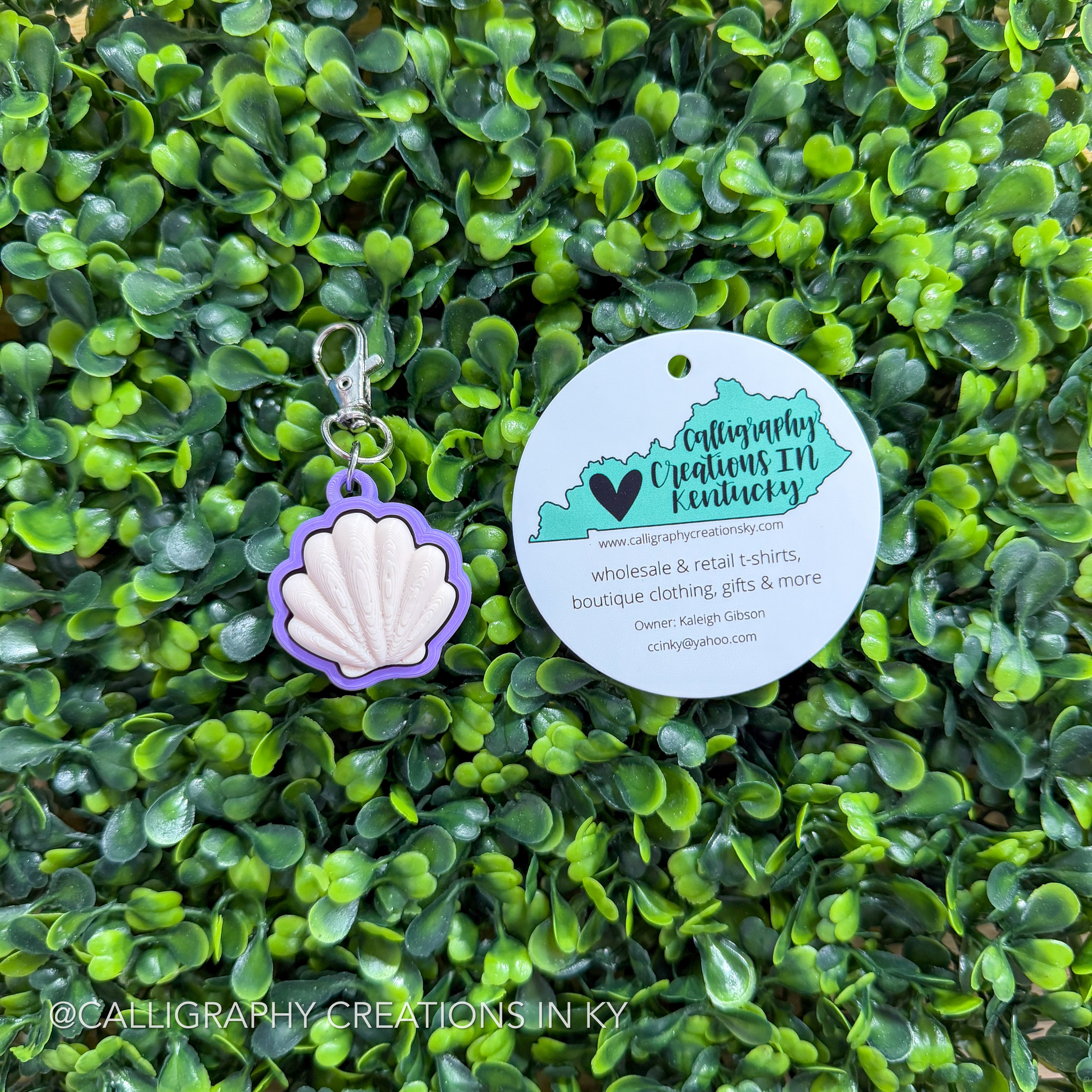 Shell-shaped fidget clicker keychain with a tag on a green leafy background
