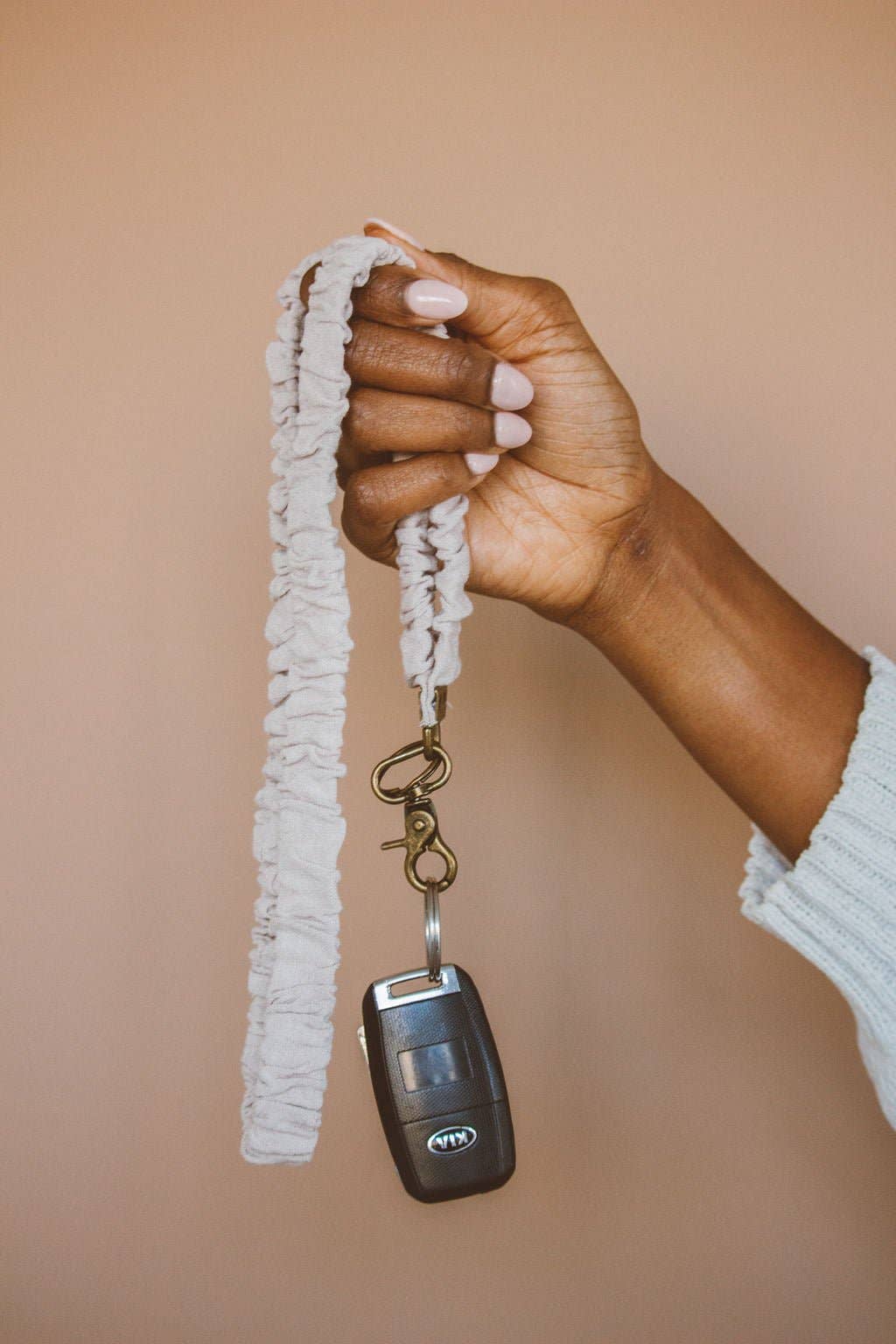 Person holding beige linen scrunchie keychain with key fob attached against a brown background 
