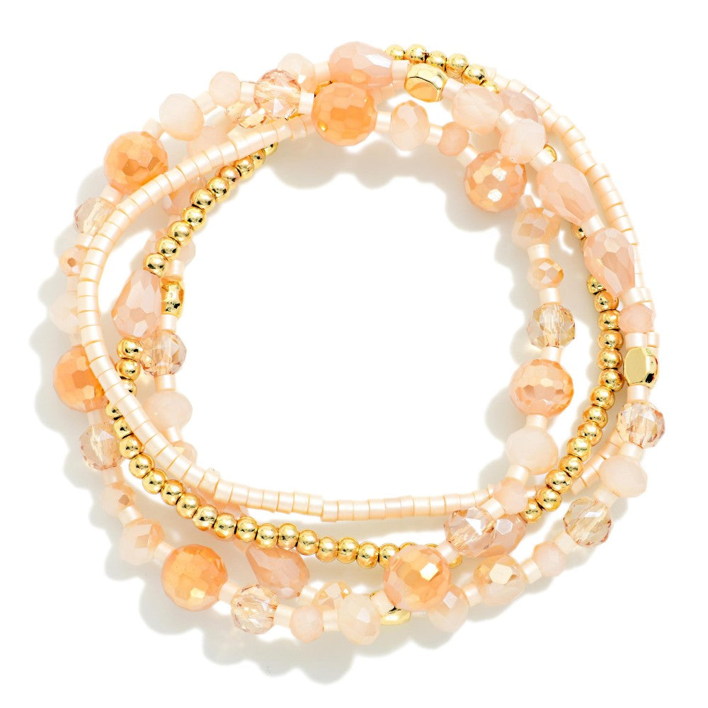 A stack of beaded stretch bracelets in peach, cream, and gold, displayed on a clean white background.