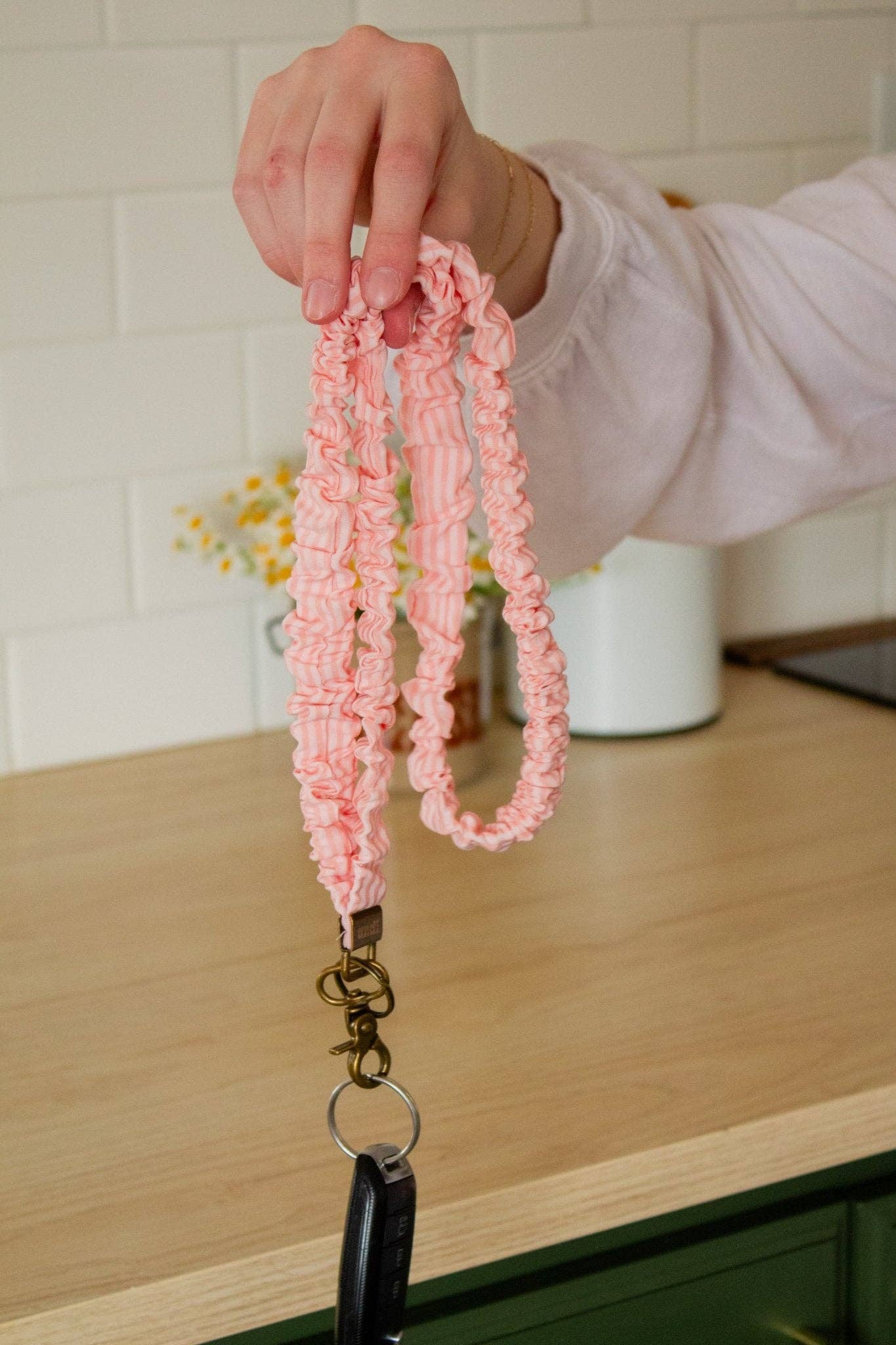 Person holding a pink striped key chain in front of a white tile background with a wooden counter 