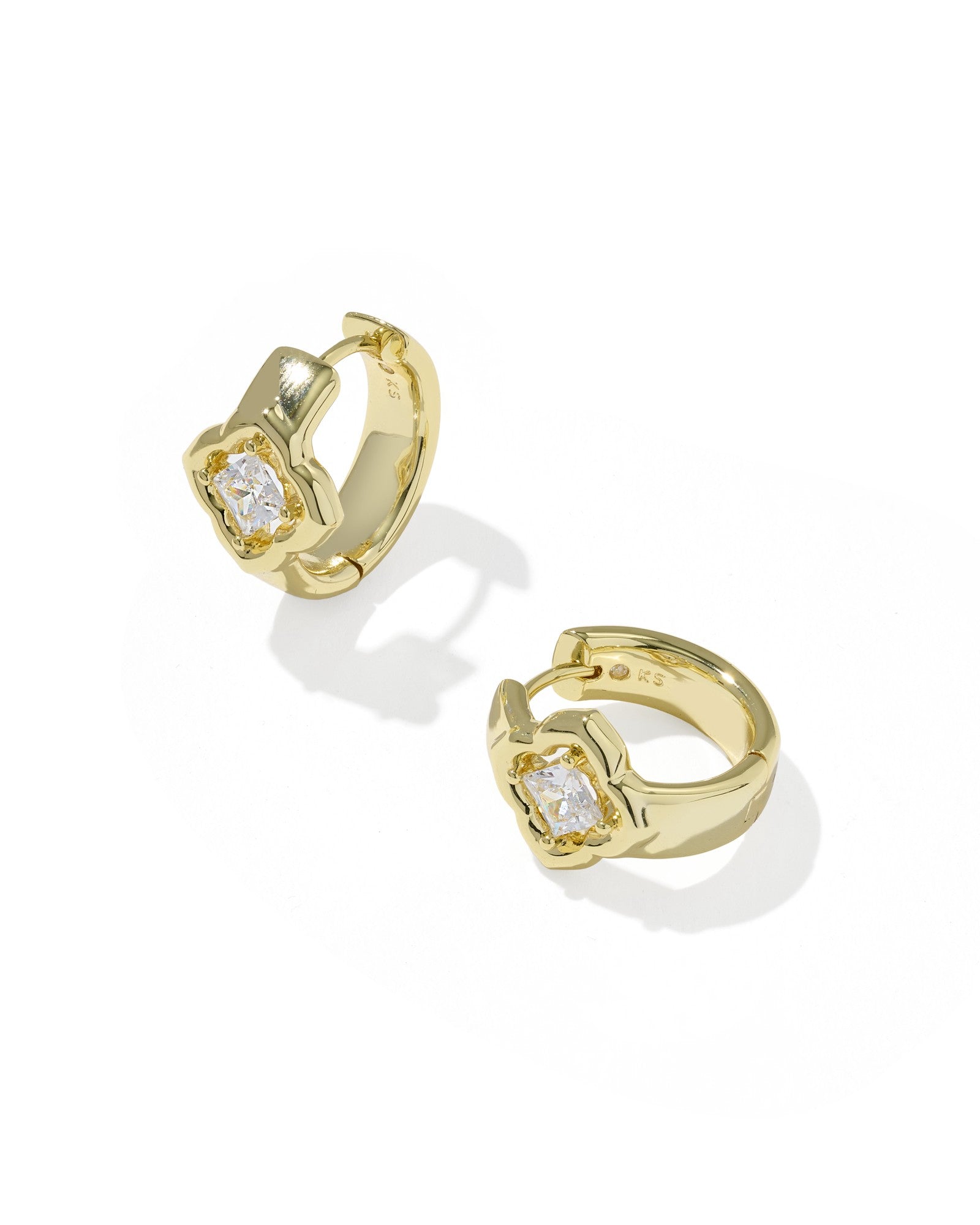 A pair of gold huggie hoop earrings with a central floral setting and a clear round-cut gemstone, shown on a clean white background with soft shadows.