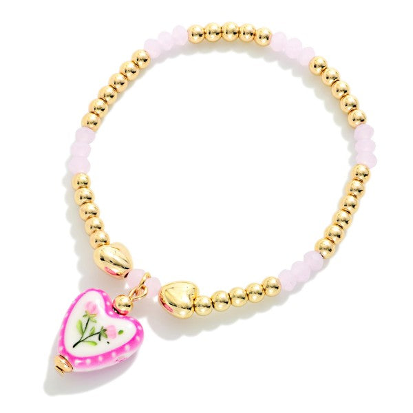 Bracelet with gold beads and a heart-shaped pink charm on a white background