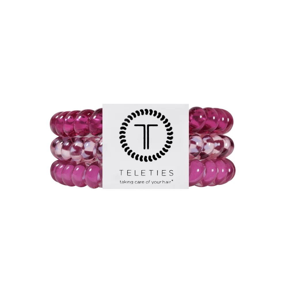 Three Teleties hair extension bands in a translucent magenta pink color, stacked together with a white paper band featuring the black Teleties logo and brand name.