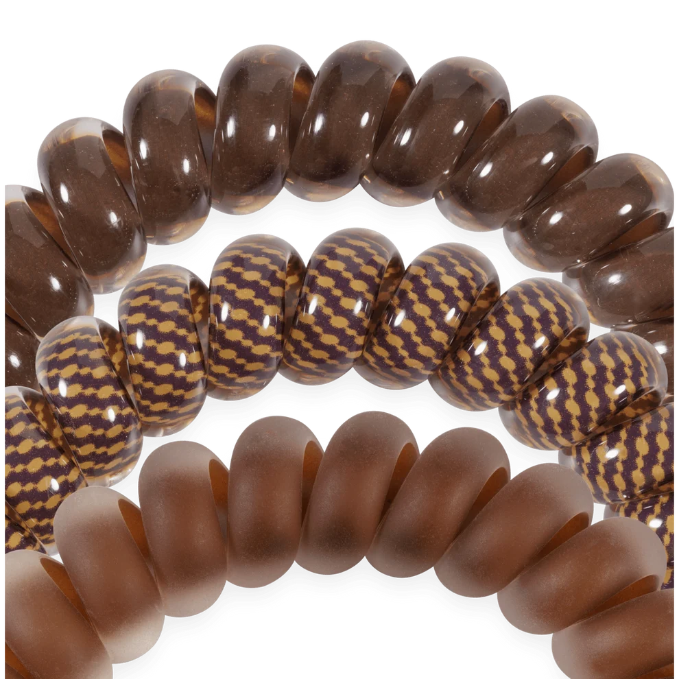Three strands of brown beaded bracelets or mala-style cords arranged in overlapping loops on a white background. The top strand has glossy dark brown oval beads, the middle strand has alternating dark brown and tan patterned round beads, and the bottom strand has smooth matte medium-brown coiled beads.
