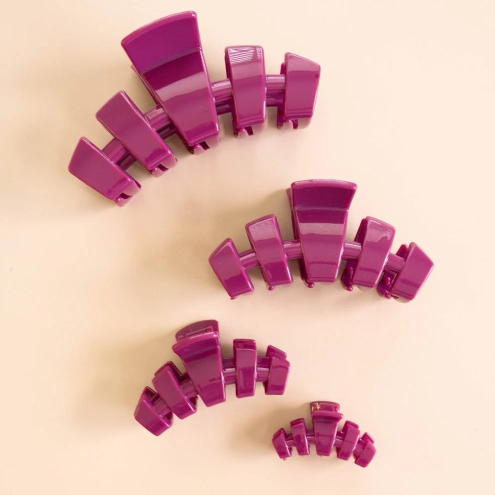 Four glossy purple hair claw clips in different sizes arranged on a light beige background.