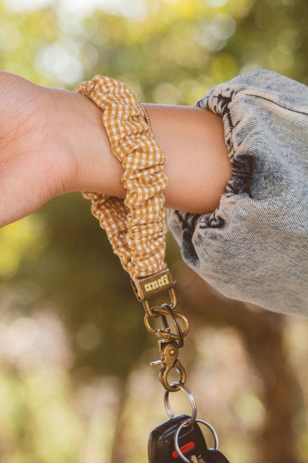 Person with Mustard gingham keychain around their wrist with a blurred background 
