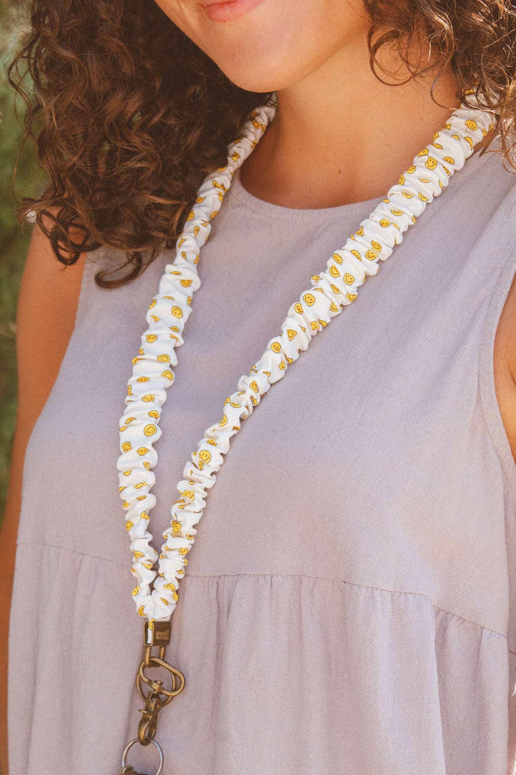 Woman in purple tank top wearing a white scrunchie lanyard with yellow happy faces  