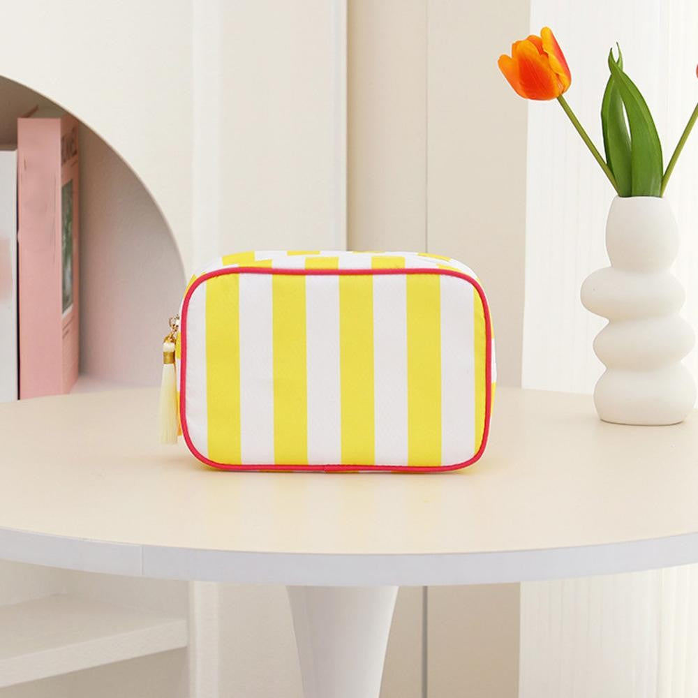 Yellow and white striped pouch on a table with a vase of flowers in the background