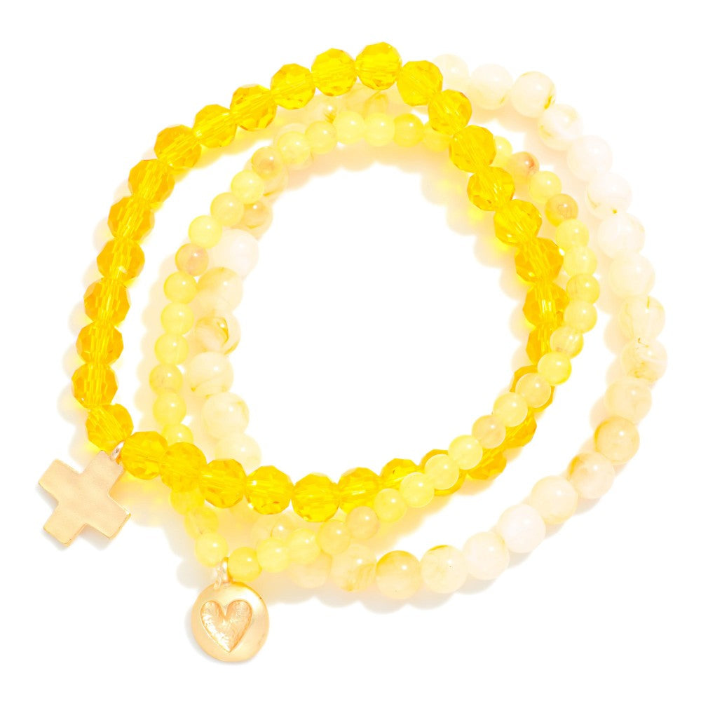 Set of yellow beaded bracelets with charms on a white background