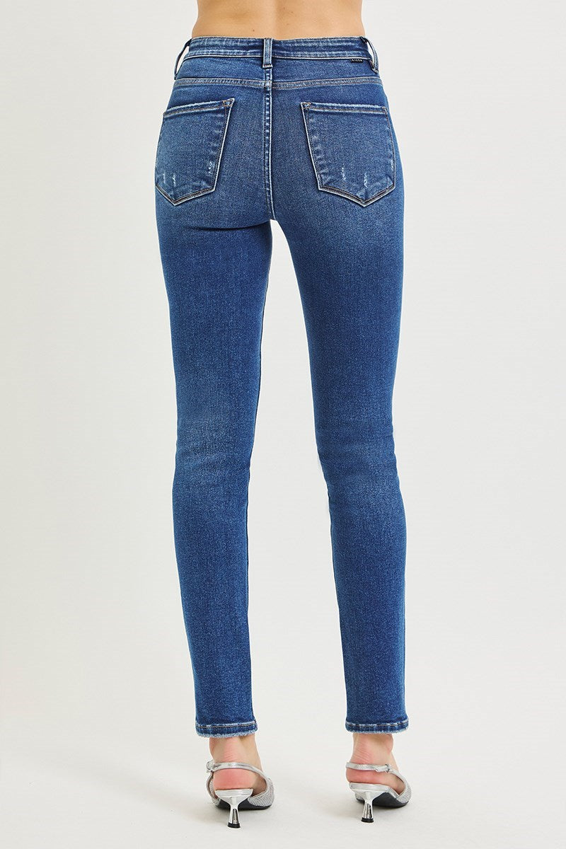 Rear view of a person wearing blue skinny jeans and metallic heeled sandals against a plain light gray studio background.