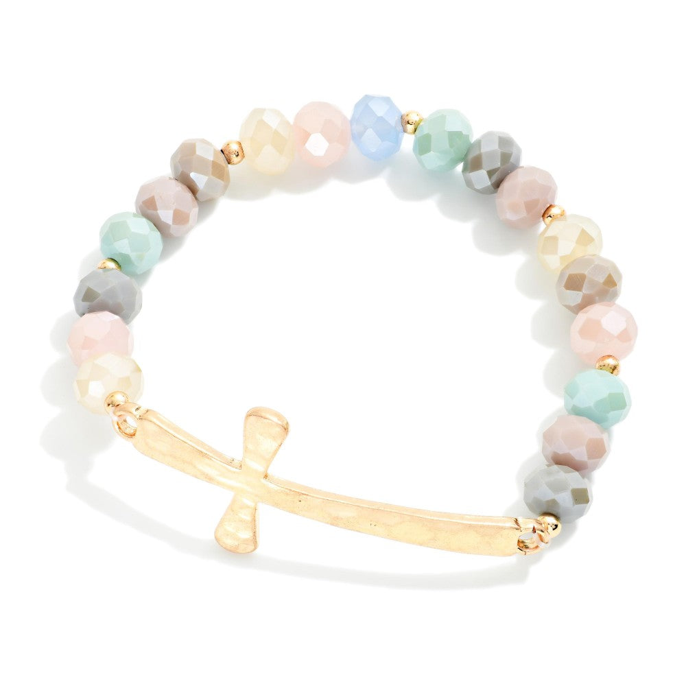 A beaded stretch bracelet featuring faceted pastel beads in pink, blue, green, gray, and cream, accented by a hammered gold bar and cross charm.