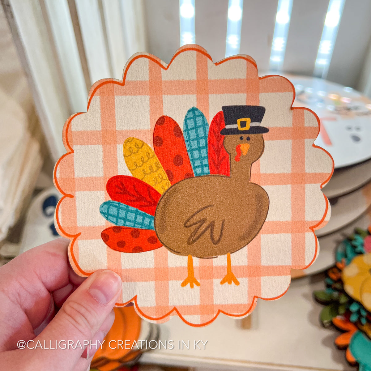 Wood cutout with a turkey design on a checkered background held by a hand.
