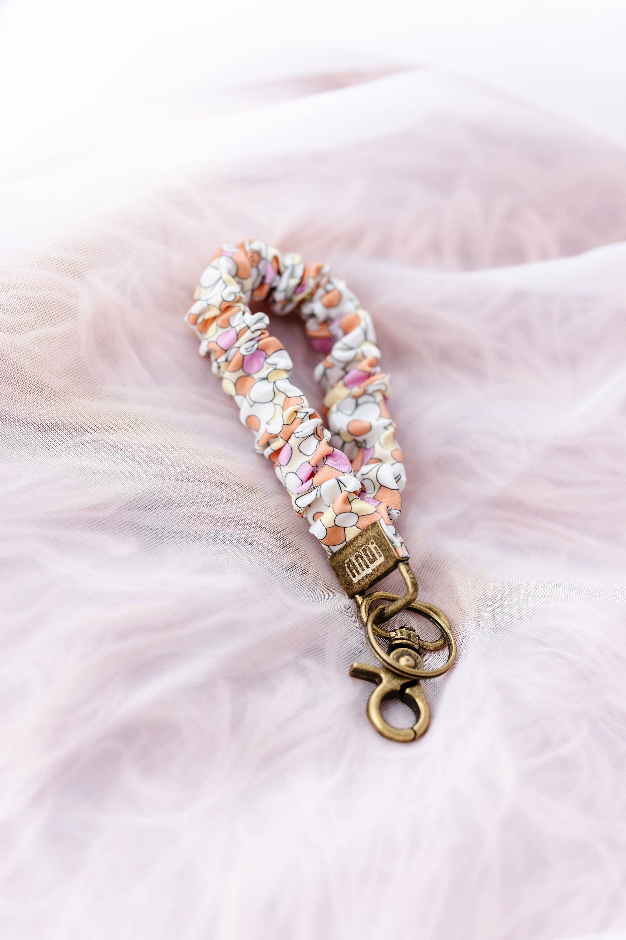 Flower patterned scrunchie key chain with gold clasp on a pink fluffy background 