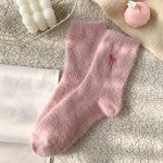 A pair of fuzzy pink socks laid flat on a light textured surface, with a small embroidered pink bow detail on one sock.