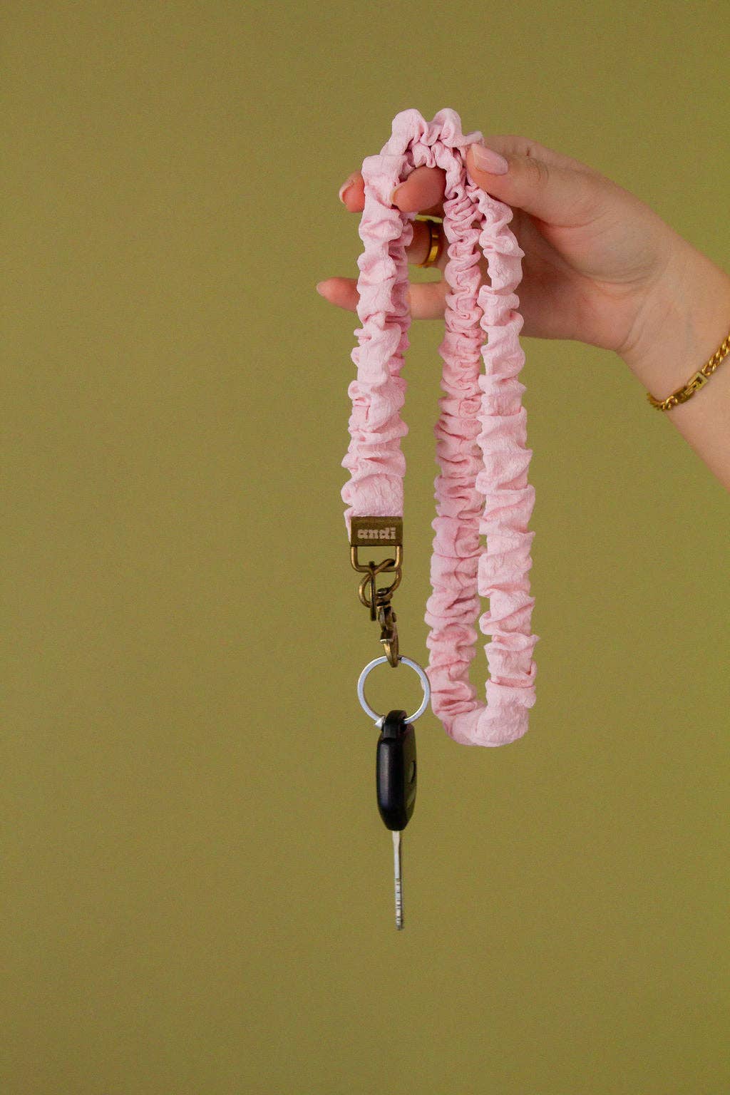 Pink ruched keychain held by a hand against a green background