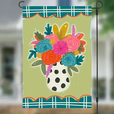 A decorative garden flag hanging from a black metal stand. The flag features a colorful floral bouquet in a white polka-dot vase against a light olive-green background, with teal plaid borders at the top and bottom.