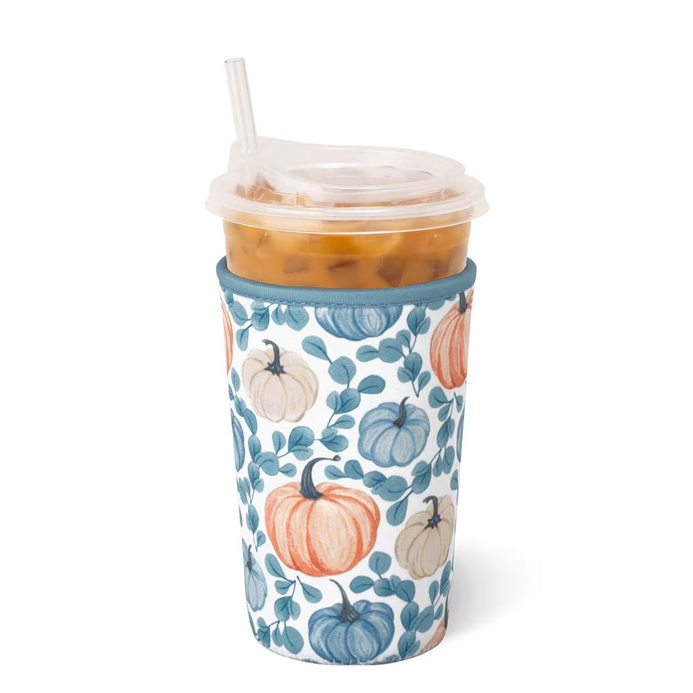A clear plastic travel tumbler with a clear lid and straw, filled with an iced orange drink, wrapped in a white fabric sleeve printed with blue leaves and orange and beige pumpkins, on a white background.