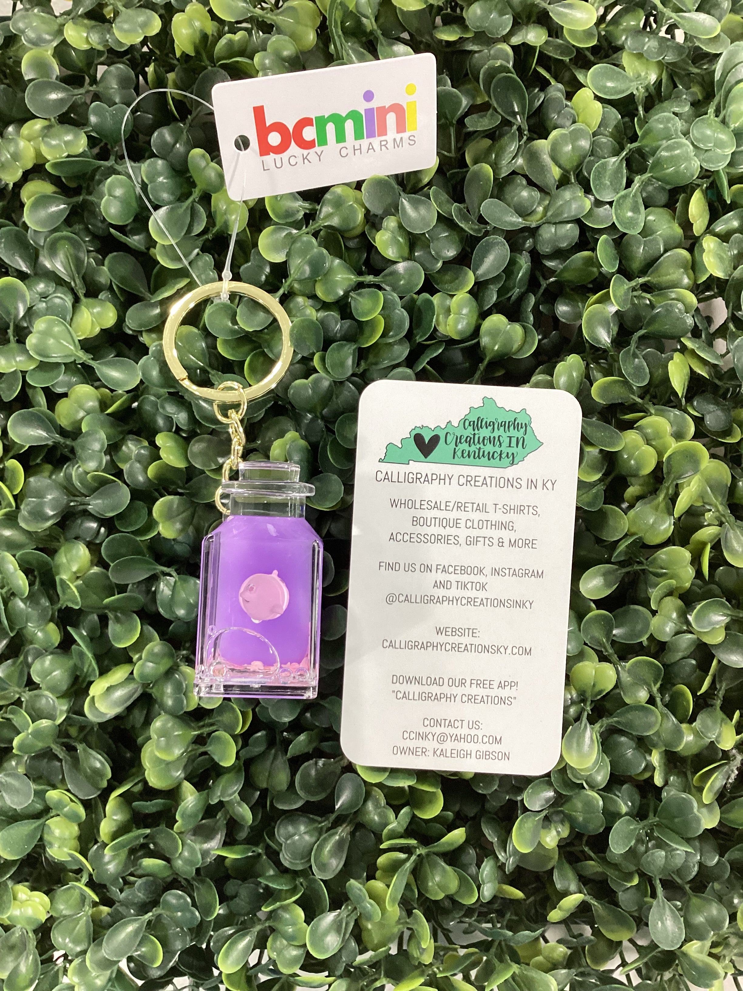 Purple keychain with a business card for size reference on a green leafy background