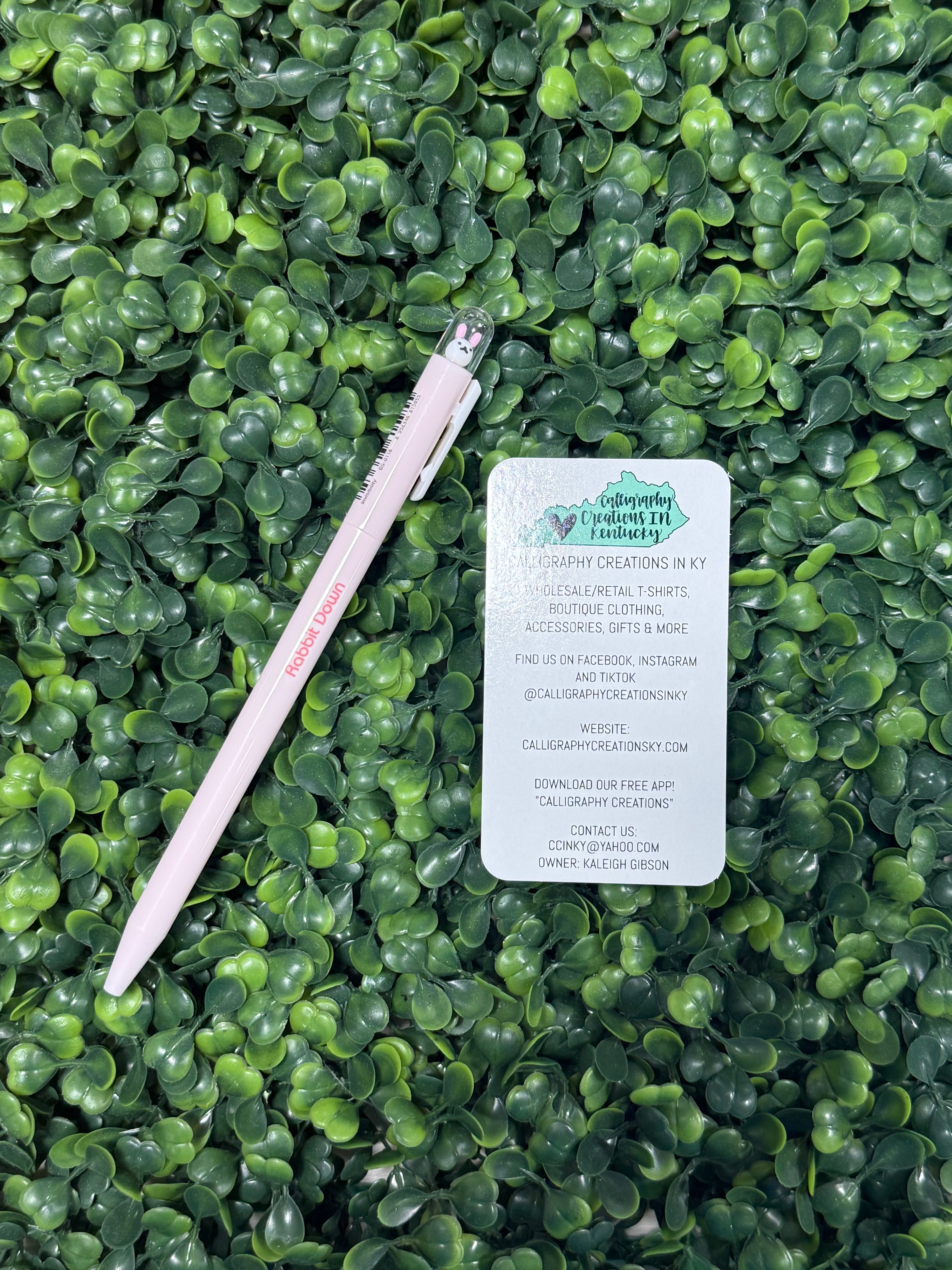 Pink pen and business card on a green leafy background