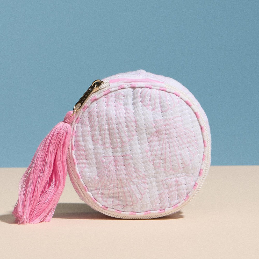 Round woven pouch with a pink tassel on a beige surface and blue background