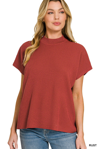 A woman wearing a rust-colored ribbed short-sleeve mock neck top and blue jeans, shown against a plain white background.