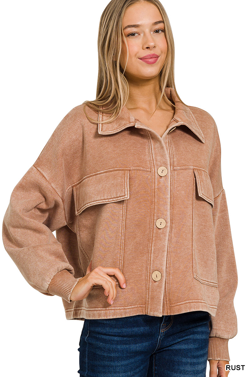 A woman wearing a rust-colored, cropped button-up jacket with a collar and front pockets, paired with blue jeans, against a plain white background.