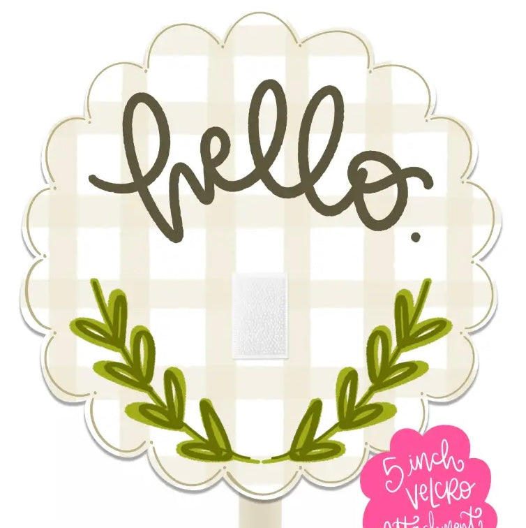 A scalloped white picket-style sign on a stick with a cream gingham background, dark brown 'hello' script, green leafy accents, and a pink '5 inch velcro attachment' sticker.