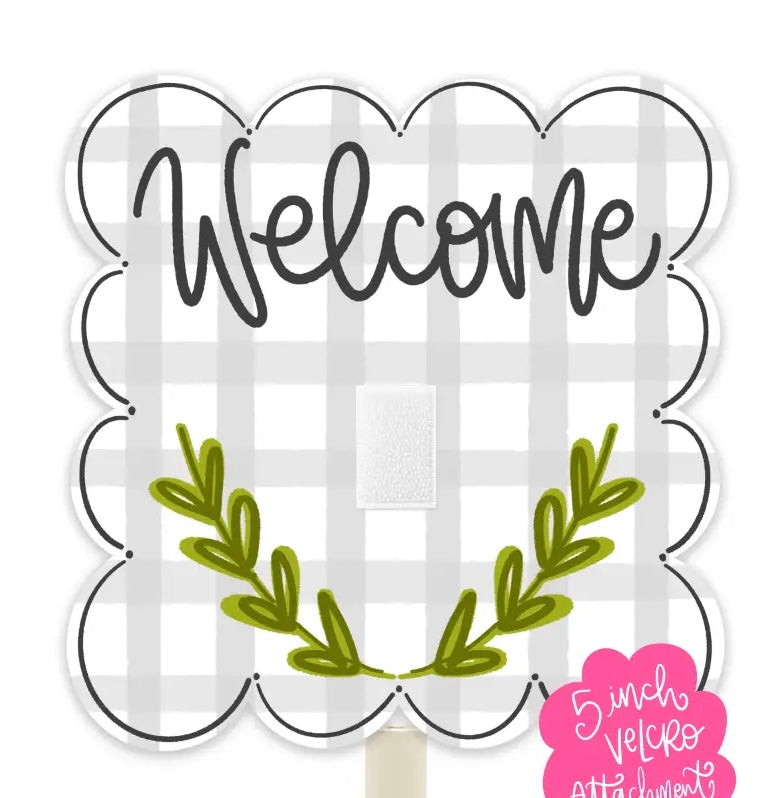 A scalloped white sign with a gray buffalo plaid background, the word 'Welcome' in black script, and an olive green leafy wreath at the bottom. A pink sticker in the lower right says '5 inch Velcro Attachment.
