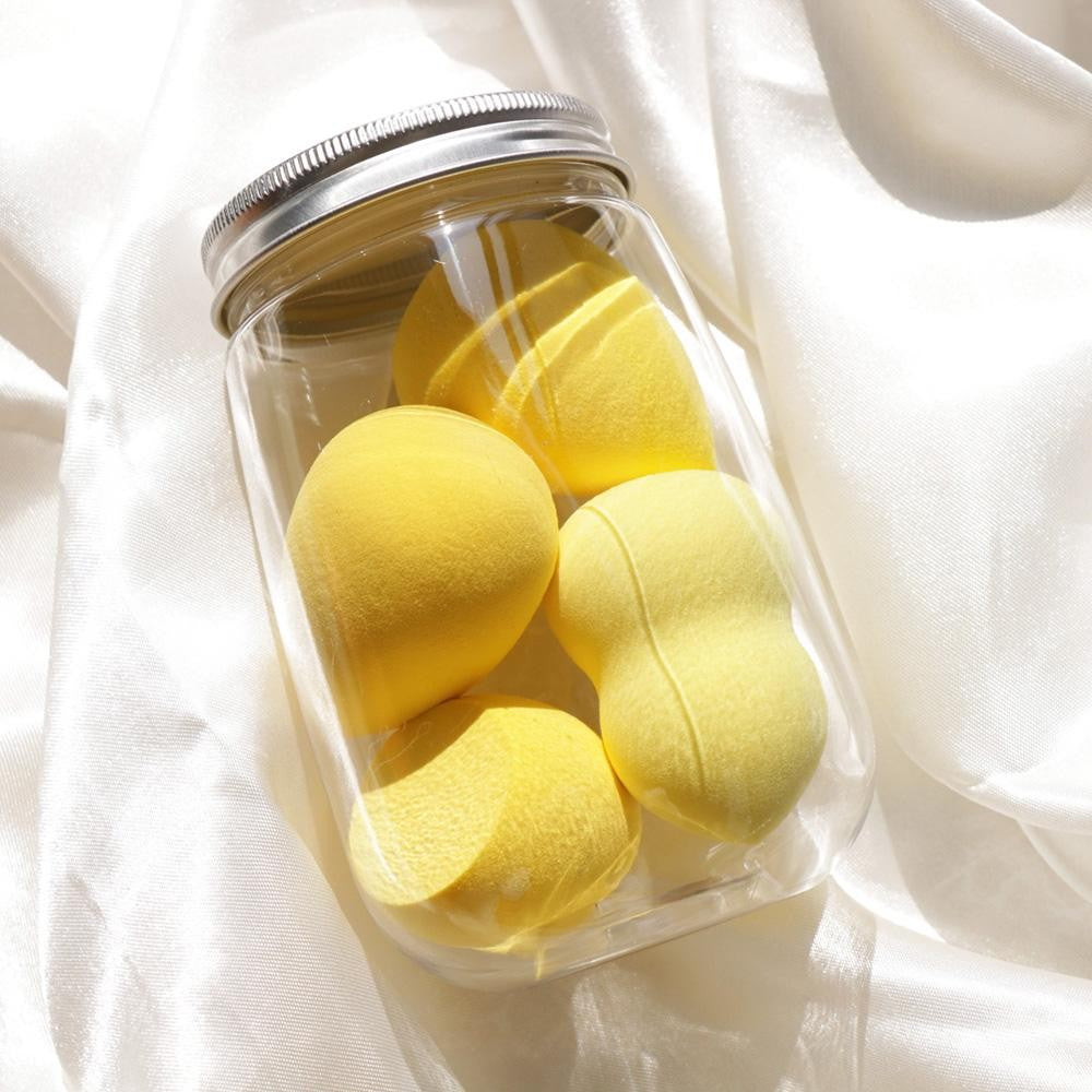 Clear jar with silver lid containing yellow bath bombs on a white fabric background