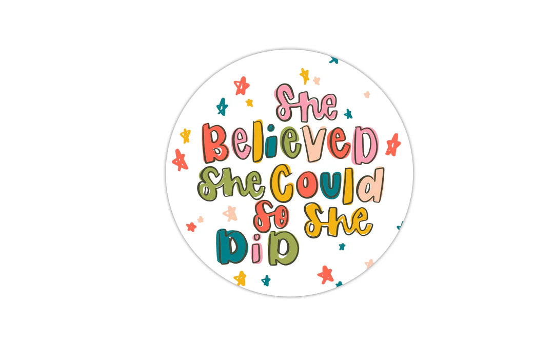 A circular sticker or decal with the motivational quote 'She Believed She Could So She Did' in colorful hand-lettered text, surrounded by small star illustrations on a white background.