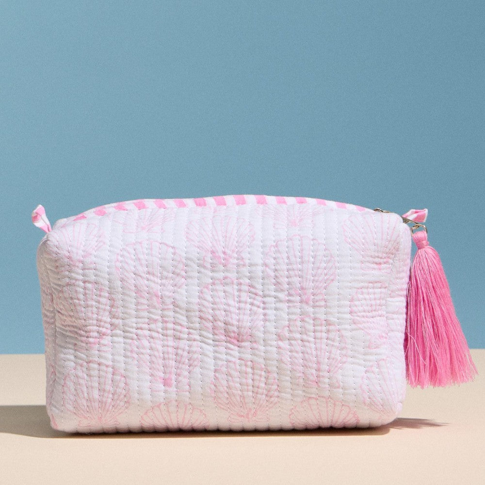 Pink textured pouch with a tassel on a beige surface and blue background