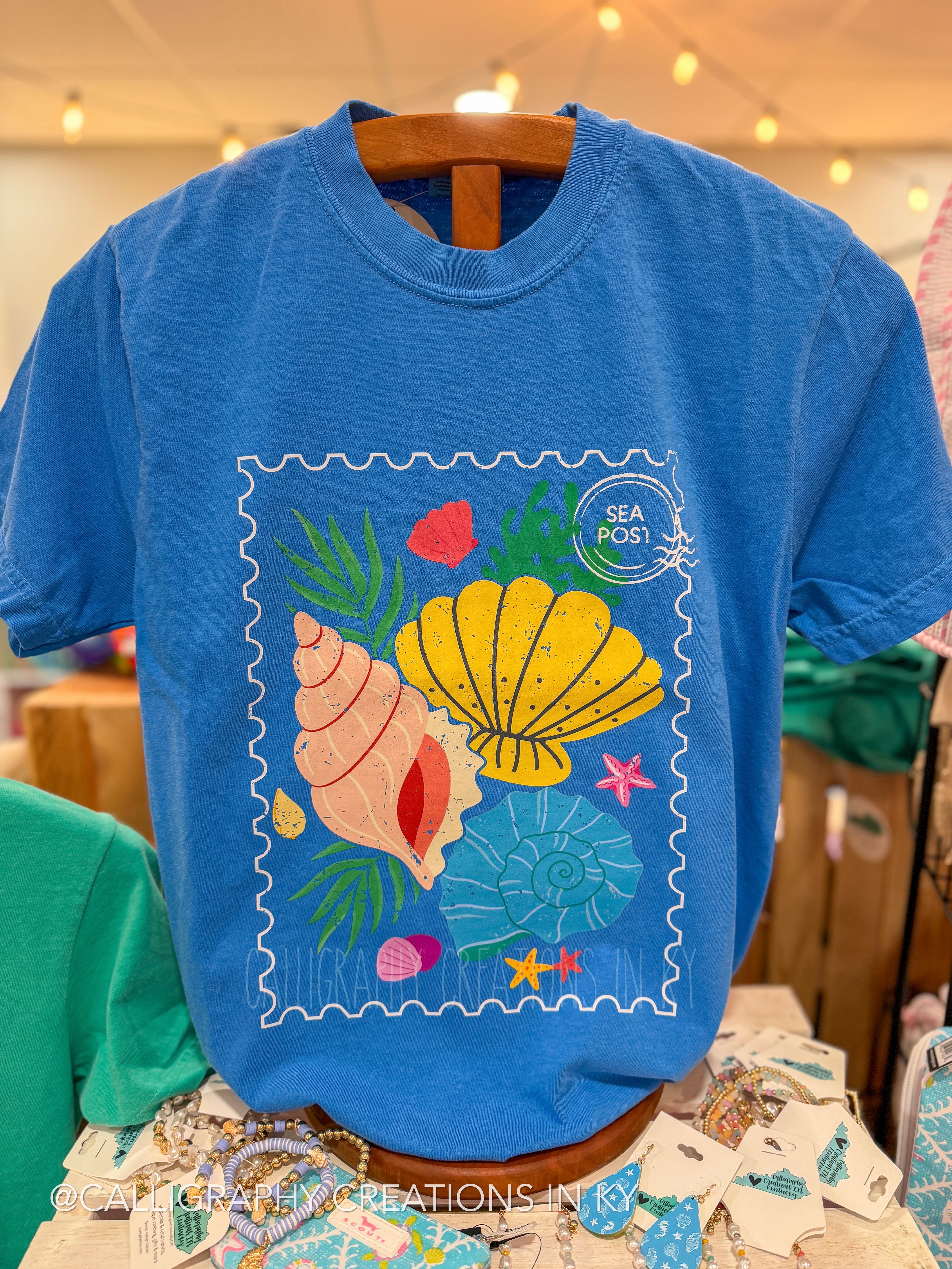 Blue t-shirt with a colorful seashell design on a hanger.