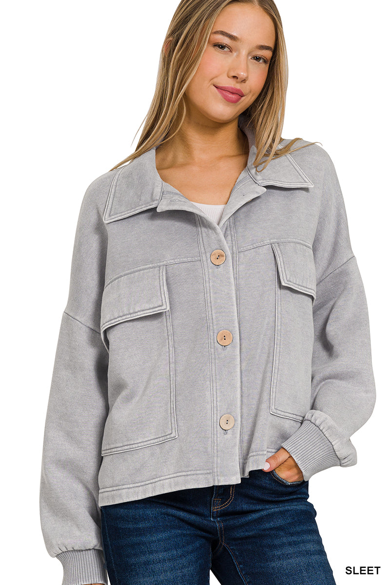 A woman wearing a light gray oversized cropped jacket with a collar, three wooden buttons, and front flap pockets, paired with dark blue jeans against a white background.