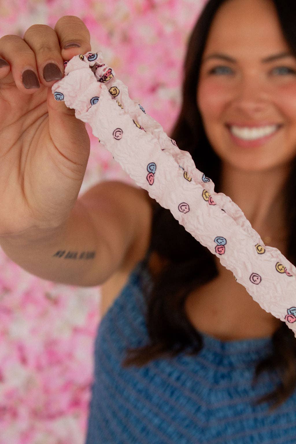 Person holding pink scrunchie key chain with happy faces on it in front of a blurred background 