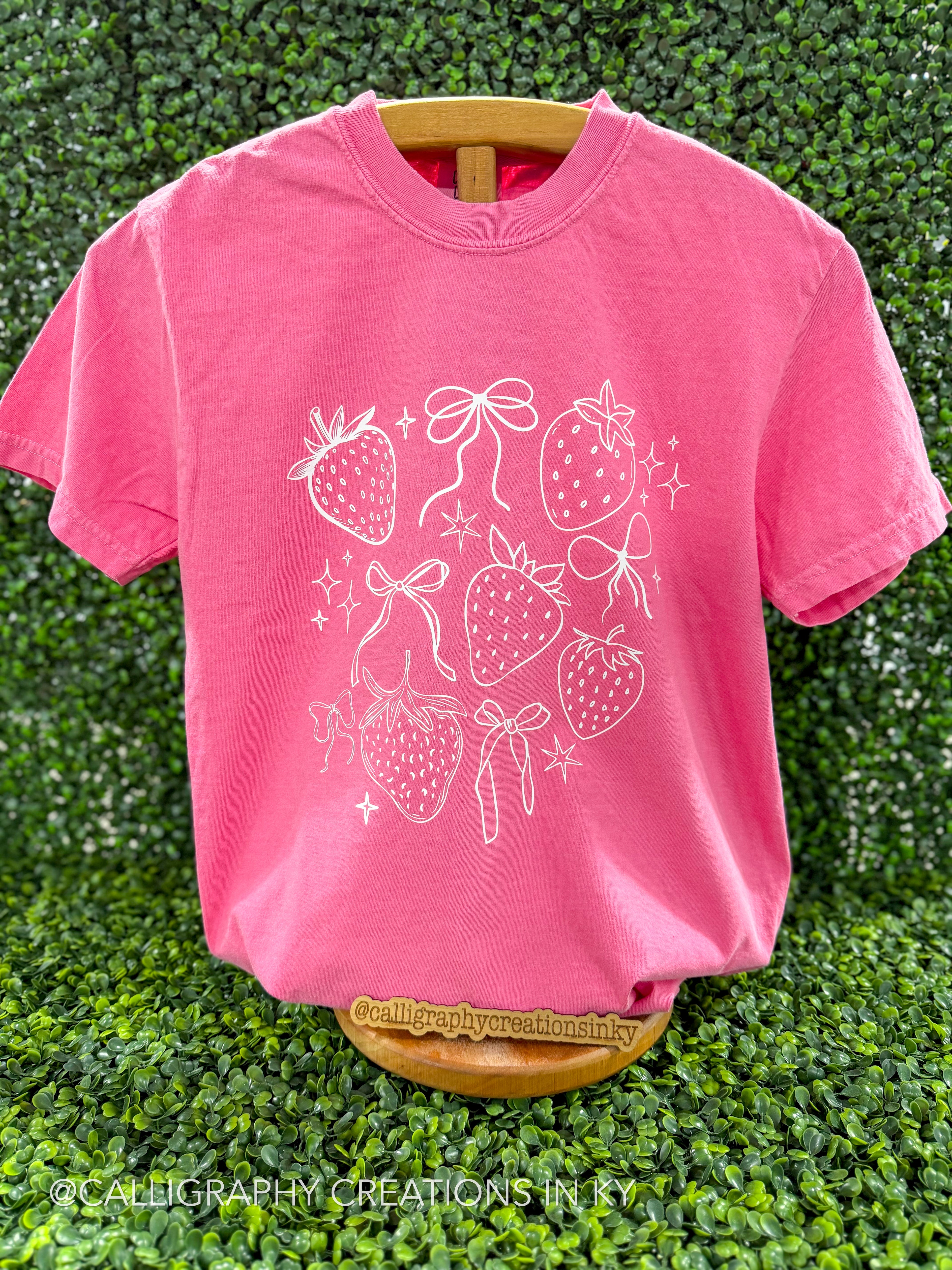 Pink shirt with strawberries and bows printed in white on a wooden stand