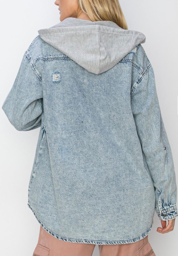 A woman viewed from the back wearing a light blue acid-wash denim hooded jacket with a gray hood and a distressed detail on the left shoulder, paired with dusty pink pants.
