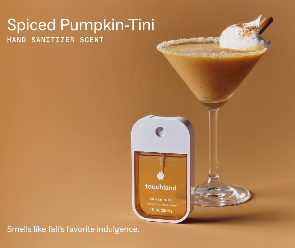 A Touchland hand sanitizer spray bottle in a white rectangular case with amber liquid, shown beside a pumpkin-tini cocktail in a martini glass on a warm tan background. Text reads 'Spiced Pumpkin-Tini' and 'HAND SANITIZER SCENT.
