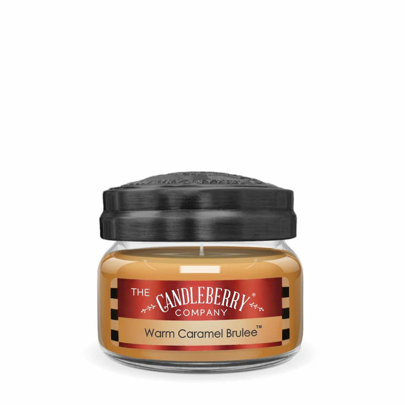 A small jar candle with a brown label reading 'Warm Caramel Brulee' and a black lid.