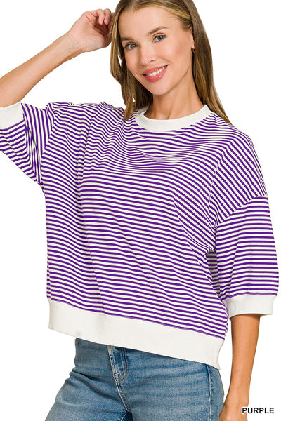 A woman wearing a purple and white horizontally striped short-sleeve top with white ribbed trim, paired with blue jeans, against a plain white background.