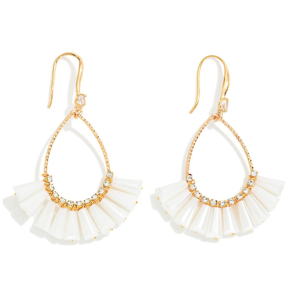 A pair of gold-tone drop earrings featuring a teardrop-shaped frame with a cascading fan of white shell-like discs and a row of clear rhinestones along the top curve, set against a plain white background.