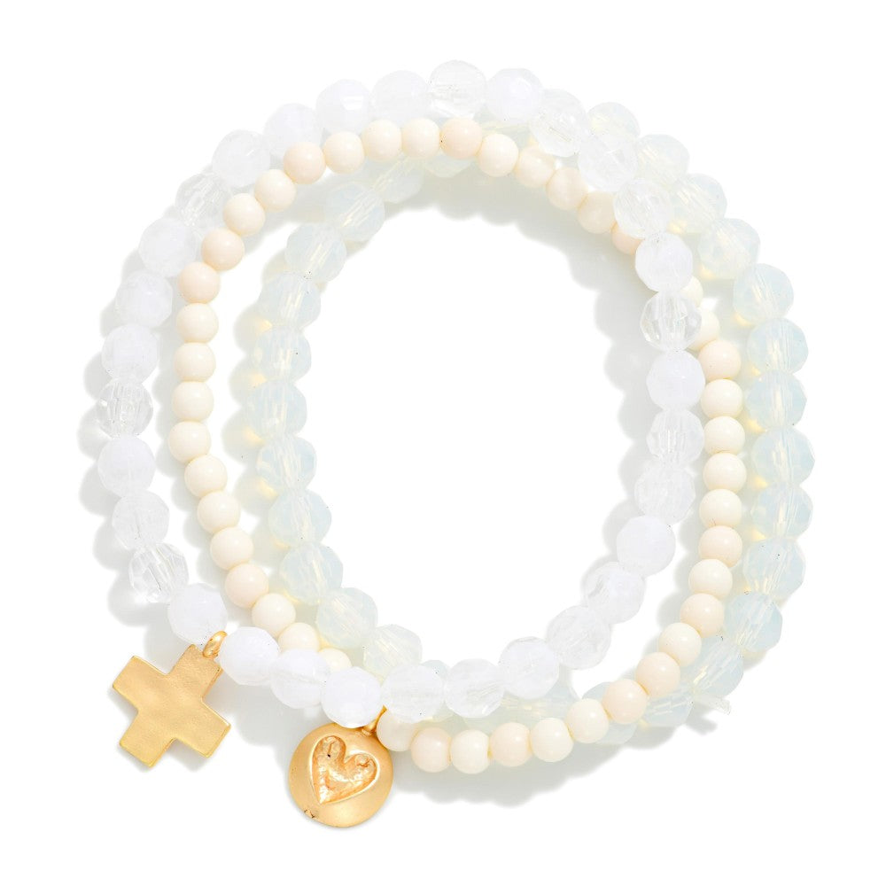 Stack of white beaded bracelets with gold charms on a white background